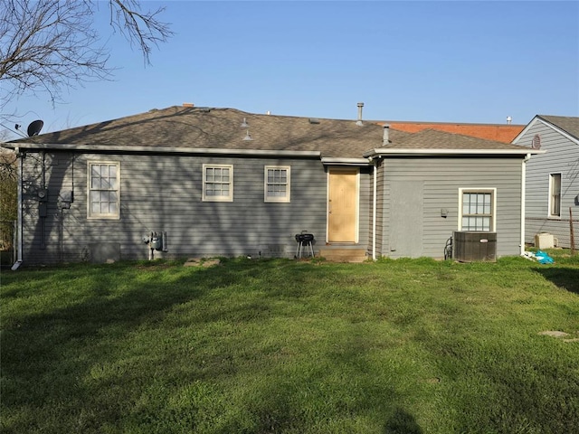 rear view of property with central AC unit, a lawn, and roof with shingles