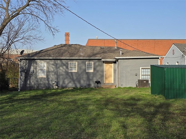 rear view of property featuring a lawn, a chimney, and a shingled roof