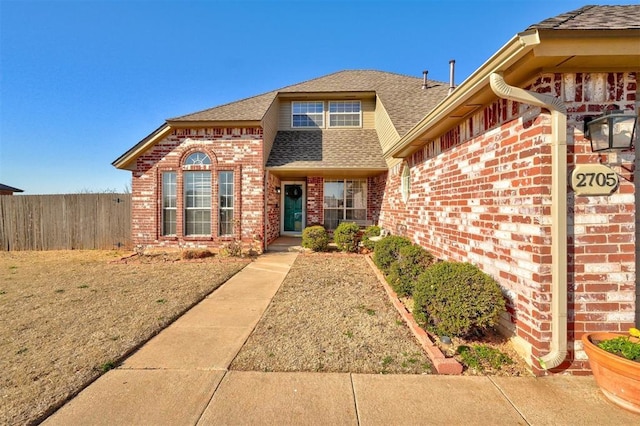 view of front of house with brick siding, a shingled roof, and fence