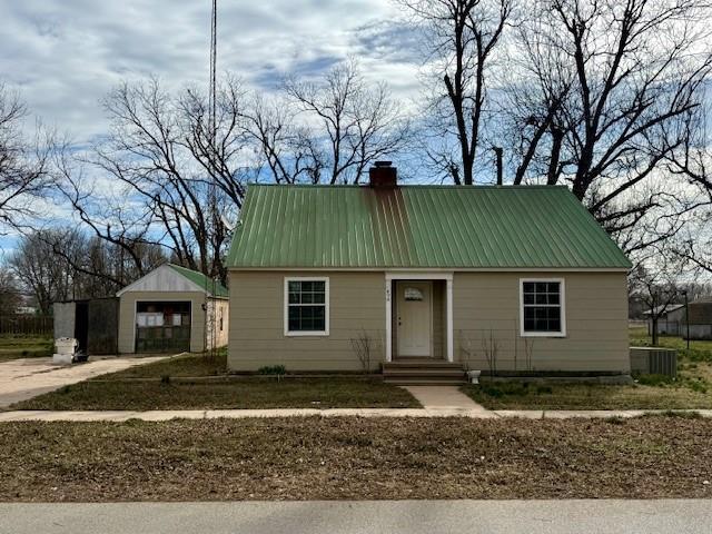 view of front facade featuring cooling unit, a chimney, concrete driveway, a detached garage, and metal roof