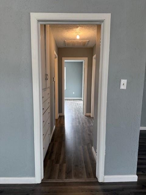 corridor with dark wood-type flooring, visible vents, baseboards, and a textured wall