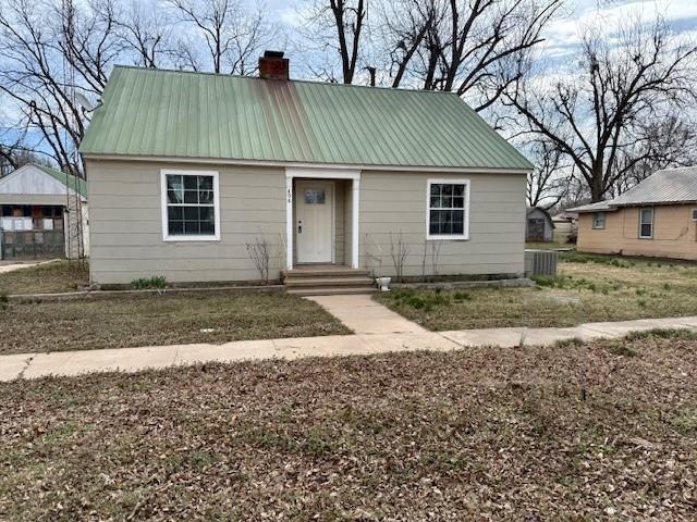 bungalow-style home with metal roof, a chimney, and central AC unit