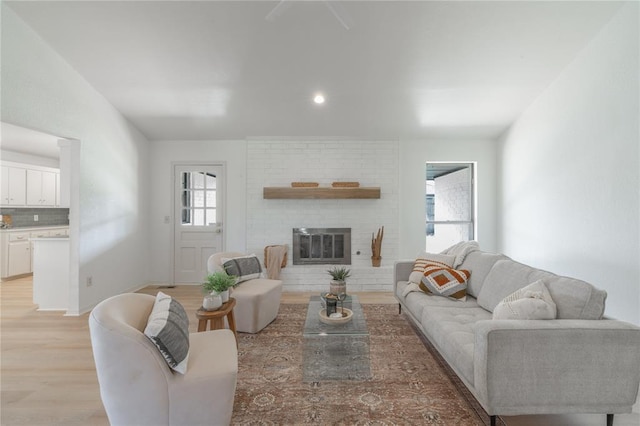 living room with a brick fireplace and light wood-style flooring