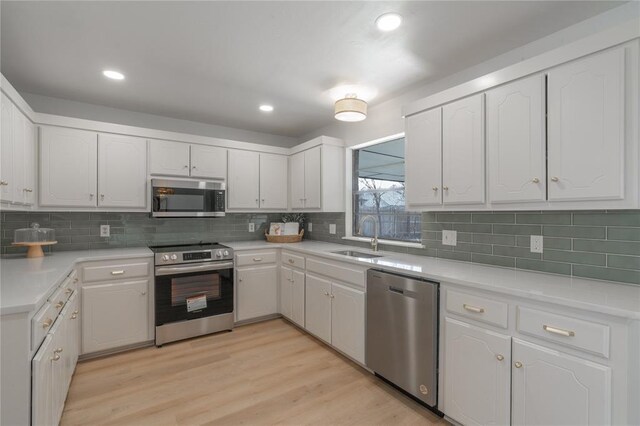 kitchen with a sink, white cabinets, light wood finished floors, and stainless steel appliances