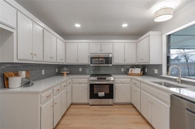 kitchen with light wood-type flooring, decorative backsplash, appliances with stainless steel finishes, white cabinets, and a sink