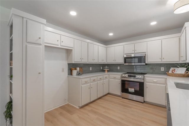 kitchen with light countertops, decorative backsplash, light wood-style flooring, appliances with stainless steel finishes, and white cabinets