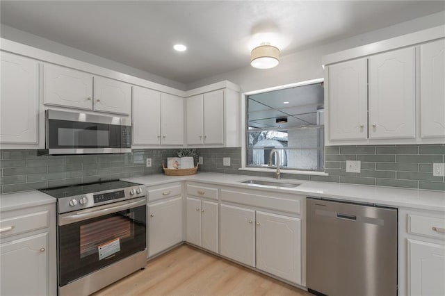 kitchen with tasteful backsplash, light wood-style flooring, stainless steel appliances, white cabinetry, and a sink