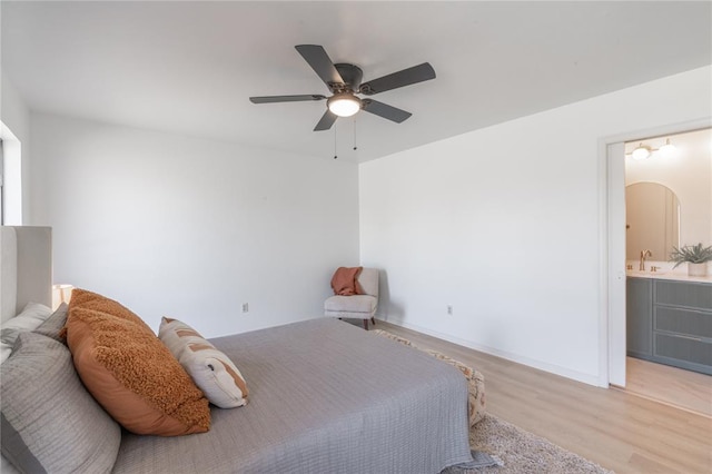 bedroom featuring light wood-style flooring, a ceiling fan, a sink, connected bathroom, and baseboards