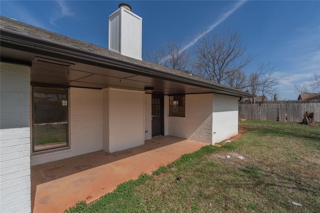 doorway to property featuring a yard, brick siding, a chimney, and fence