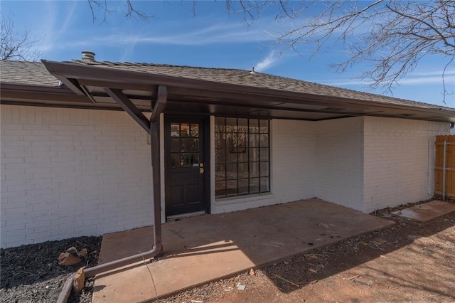 property entrance featuring brick siding, a patio area, and roof with shingles