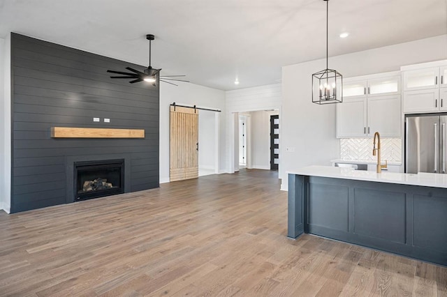 kitchen with open floor plan, a barn door, light wood-style floors, stainless steel refrigerator, and white cabinets