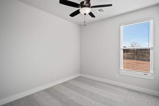 carpeted spare room featuring a wealth of natural light, visible vents, baseboards, and a ceiling fan