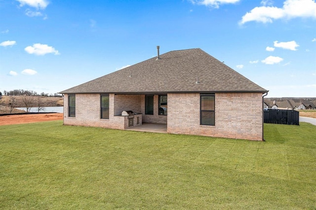 back of house featuring a lawn, area for grilling, a patio, roof with shingles, and brick siding