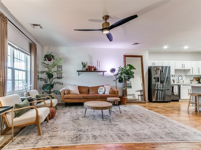 living area with light wood-style flooring, visible vents, and ceiling fan