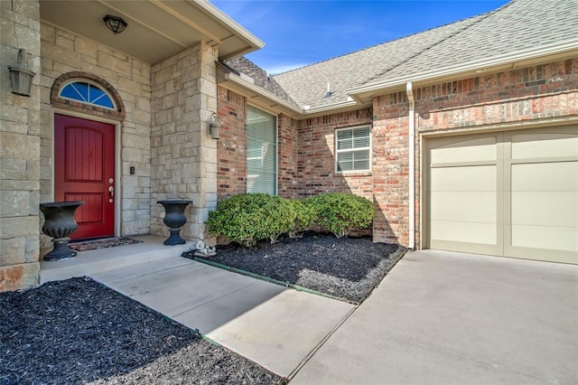 property entrance with brick siding, a garage, driveway, and a shingled roof