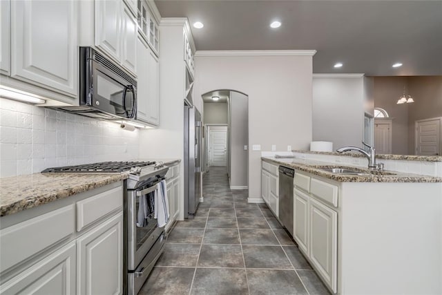 kitchen with a peninsula, arched walkways, a sink, appliances with stainless steel finishes, and tasteful backsplash