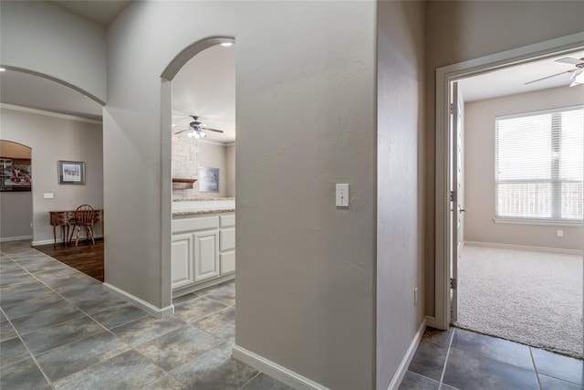 corridor featuring baseboards, arched walkways, and carpet