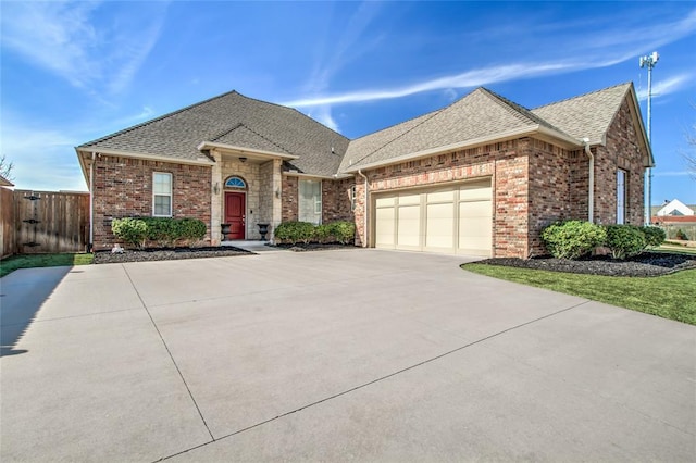 view of front of property featuring brick siding, an attached garage, fence, roof with shingles, and driveway