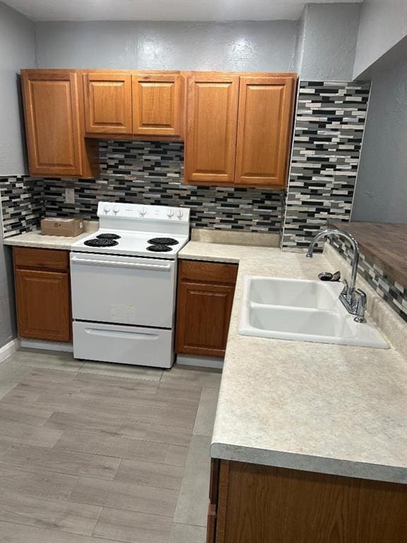 kitchen with a sink, white range with electric cooktop, light countertops, brown cabinetry, and backsplash