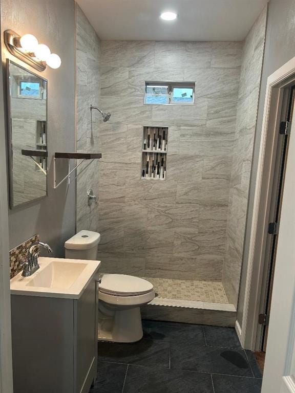 full bathroom featuring toilet, tile patterned floors, a tile shower, and vanity