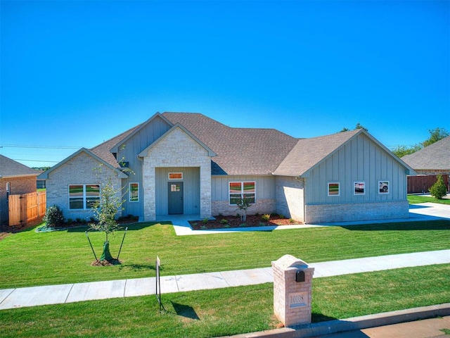 view of front of home featuring a front lawn, stone siding, fence, board and batten siding, and a shingled roof