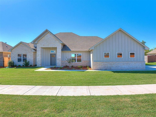 view of front of home featuring brick siding, board and batten siding, a front lawn, and roof with shingles