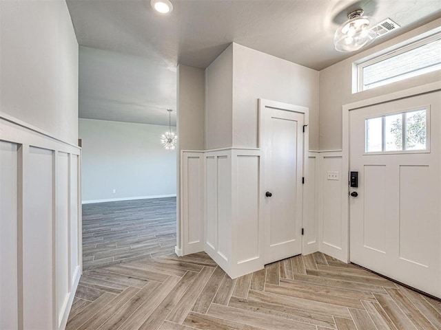 foyer featuring a notable chandelier, a decorative wall, and wainscoting