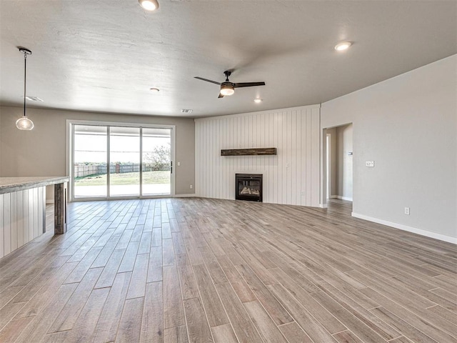 unfurnished living room featuring a glass covered fireplace, a ceiling fan, light wood-type flooring, and baseboards