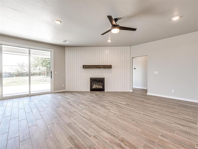 unfurnished living room with visible vents, a glass covered fireplace, light wood finished floors, baseboards, and ceiling fan