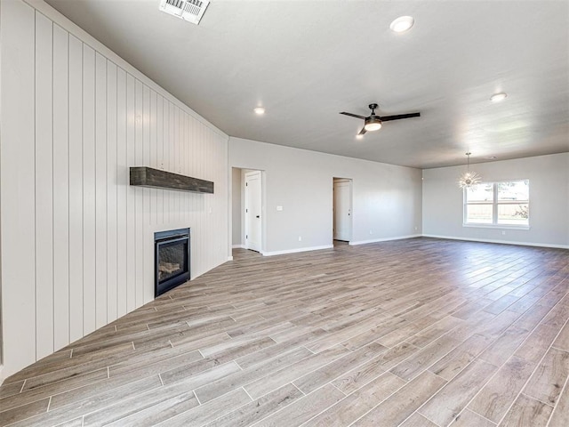 unfurnished living room featuring baseboards, visible vents, light wood-style flooring, ceiling fan with notable chandelier, and a large fireplace