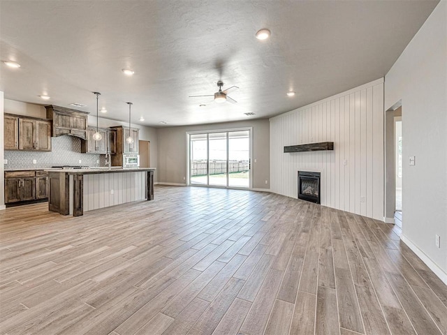 unfurnished living room featuring a fireplace, baseboards, light wood-style floors, and ceiling fan