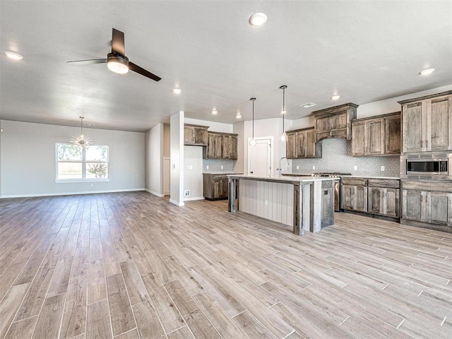 kitchen with open floor plan, decorative backsplash, light wood-style flooring, ceiling fan with notable chandelier, and stainless steel appliances