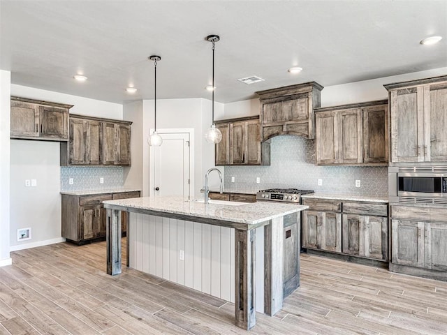 kitchen featuring light stone countertops, a center island with sink, appliances with stainless steel finishes, light wood-style floors, and a sink