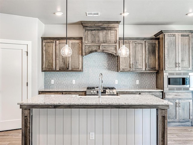 kitchen featuring stainless steel microwave, visible vents, light wood-type flooring, light stone counters, and decorative backsplash