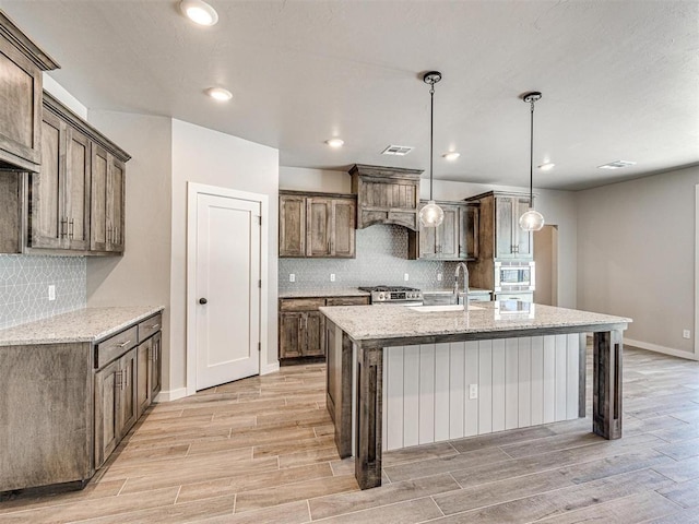 kitchen featuring a sink, light stone countertops, appliances with stainless steel finishes, and light wood-style flooring