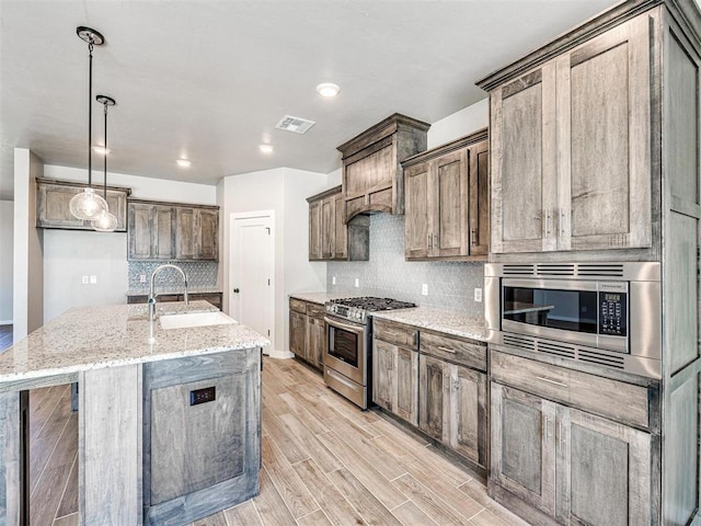 kitchen with light stone countertops, light wood finished floors, a sink, stainless steel appliances, and tasteful backsplash