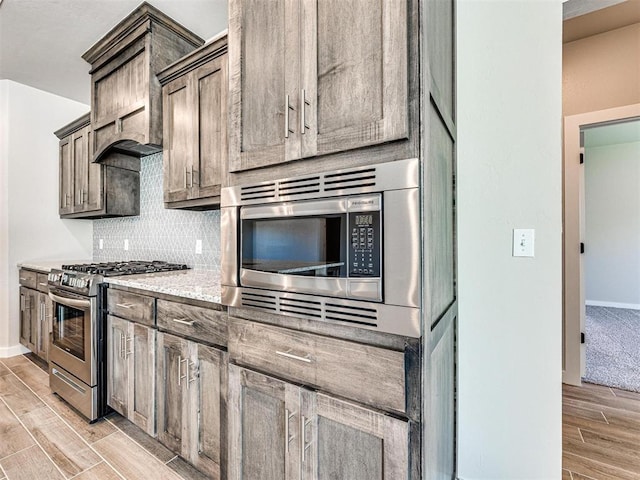 kitchen with backsplash, baseboards, wood finish floors, light stone counters, and stainless steel appliances