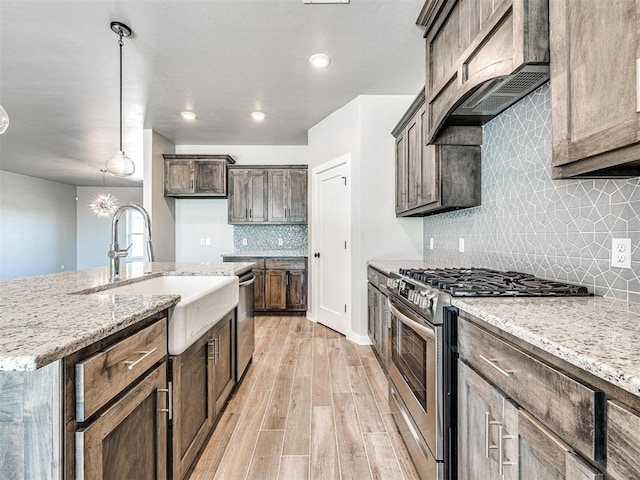 kitchen featuring light stone countertops, premium range hood, light wood-type flooring, stainless steel appliances, and a sink