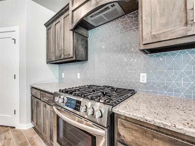 kitchen with wood finish floors, light stone counters, gas stove, exhaust hood, and decorative backsplash