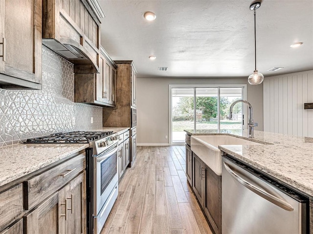 kitchen featuring backsplash, light stone countertops, light wood-type flooring, and appliances with stainless steel finishes