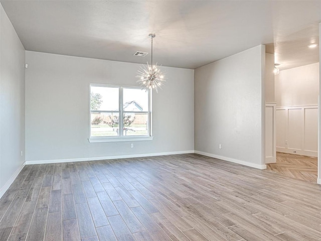 spare room with visible vents, baseboards, an inviting chandelier, and light wood-style flooring