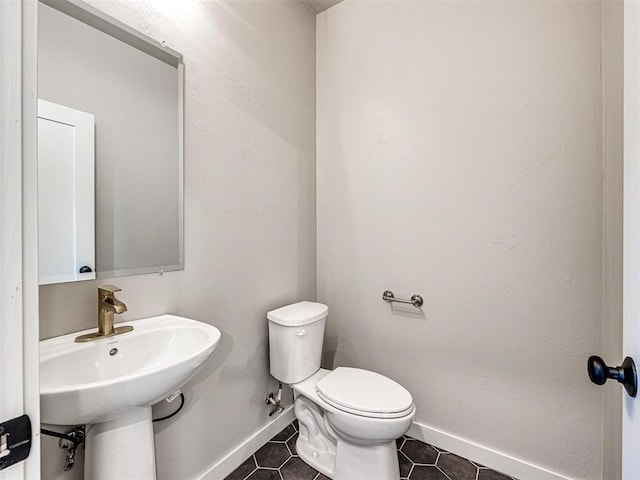 bathroom featuring tile patterned flooring, toilet, baseboards, and a sink