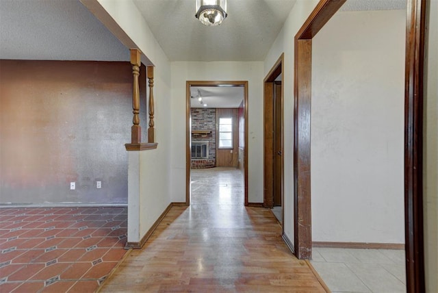 corridor featuring baseboards, a textured ceiling, and light wood-style flooring