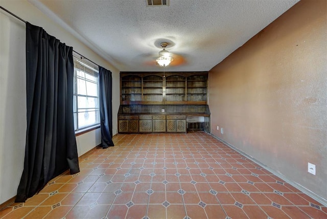 tiled empty room featuring built in features, baseboards, visible vents, and a textured ceiling