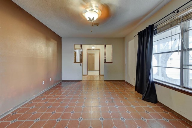 unfurnished room featuring tile patterned floors, visible vents, a textured ceiling, and a healthy amount of sunlight