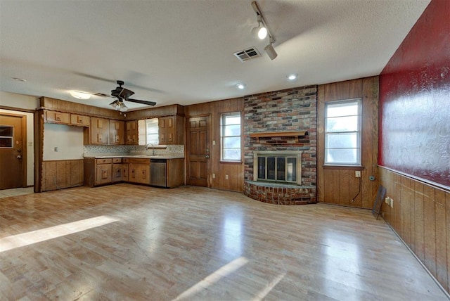 kitchen with a wainscoted wall, light wood finished floors, visible vents, wood walls, and dishwasher