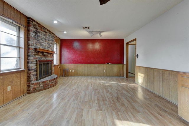 unfurnished living room with wooden walls, visible vents, a brick fireplace, a wainscoted wall, and wood finished floors