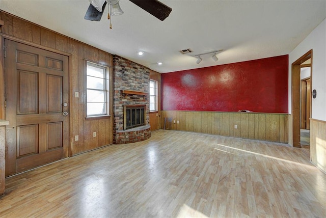 unfurnished living room with visible vents, a wainscoted wall, wood finished floors, a fireplace, and ceiling fan