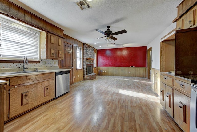 kitchen with a ceiling fan, light wood-style flooring, a fireplace, a sink, and stainless steel dishwasher