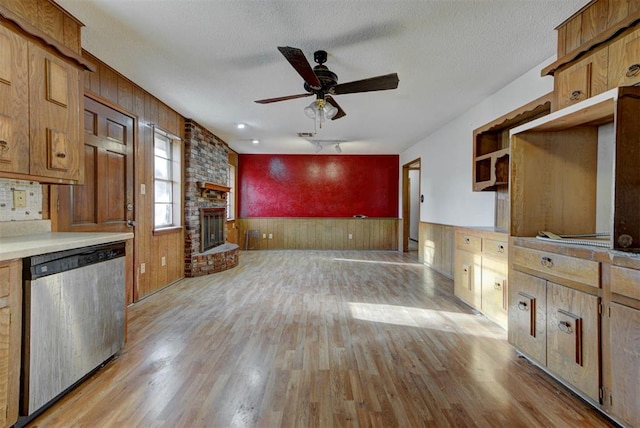 kitchen featuring light wood finished floors, wainscoting, a textured ceiling, a ceiling fan, and stainless steel dishwasher